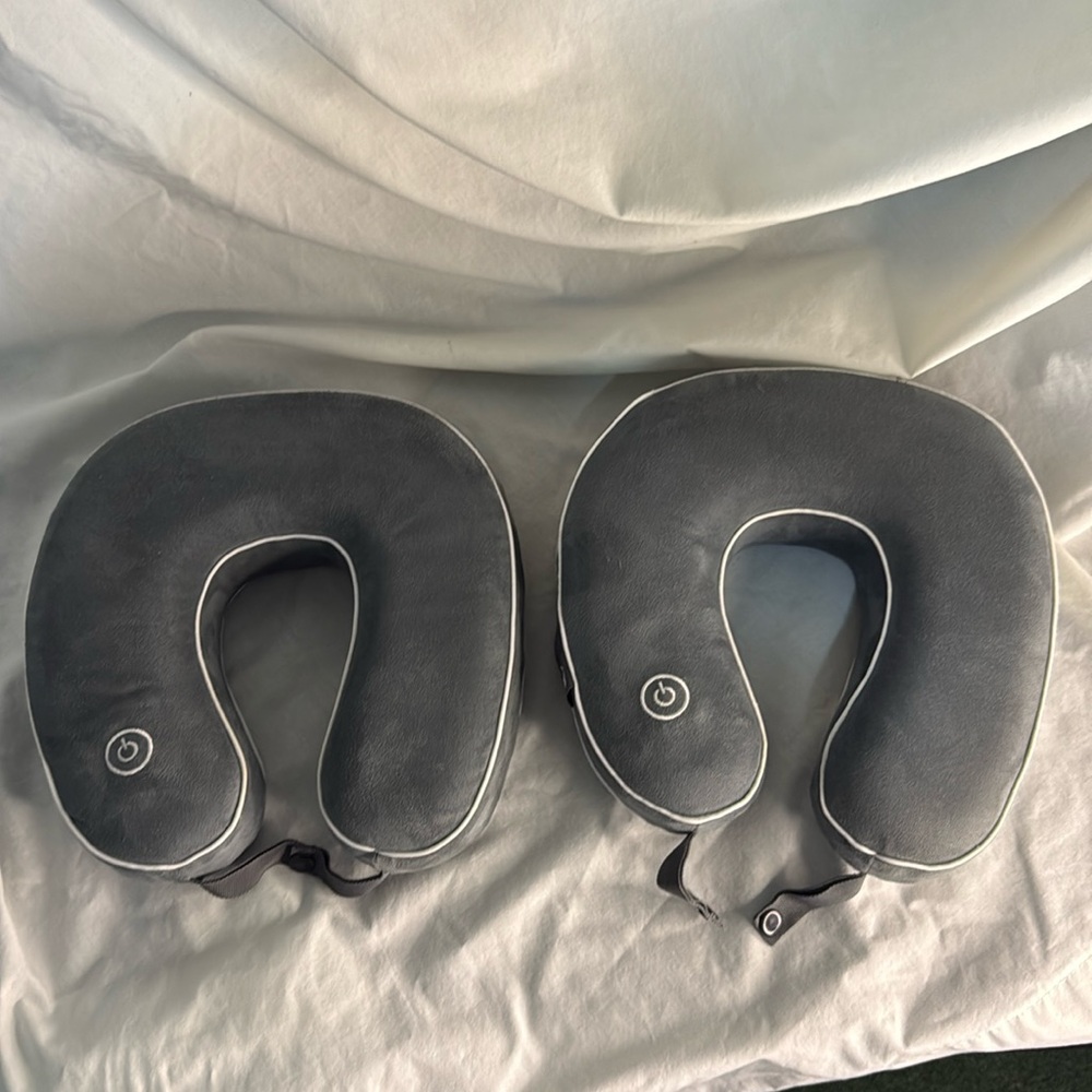 Two Gray Travel Neck Pillows with  Massage Power Button and ear plugs.